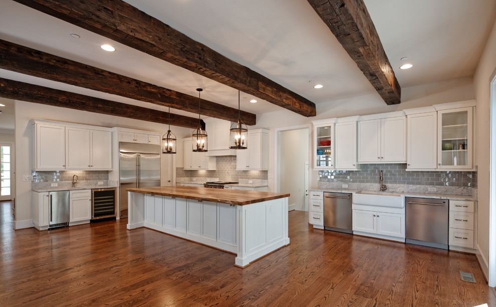 Design ideas for a large country l-shaped kitchen in Baltimore with a farmhouse sink, shaker cabinets, white cabinets, marble benchtops, grey splashback, ceramic splashback, stainless steel appliances, medium hardwood floors, with island, brown floor and grey benchtop.