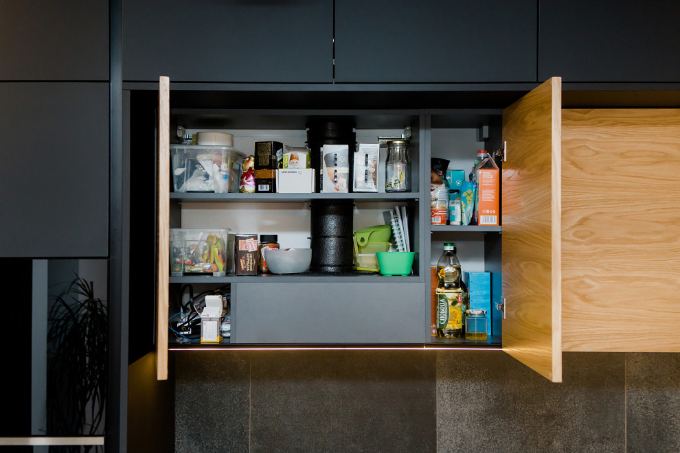 This is an example of a mid-sized contemporary single-wall kitchen in Other with solid surface benchtops, grey splashback, black appliances and ceramic floors.