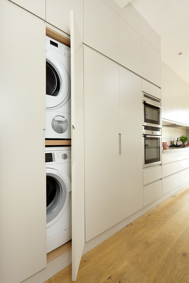 Inspiration for a contemporary laundry cupboard in London with flat-panel cabinets, beige cabinets and a stacked washer and dryer.