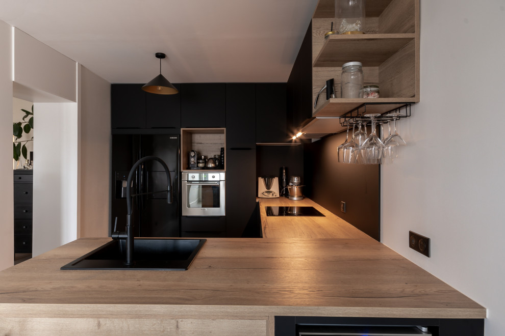 Inspiration for a mid-sized contemporary u-shaped kitchen in Lyon with a drop-in sink, flat-panel cabinets, black cabinets, wood benchtops, black splashback, porcelain splashback, black appliances and beige benchtop.