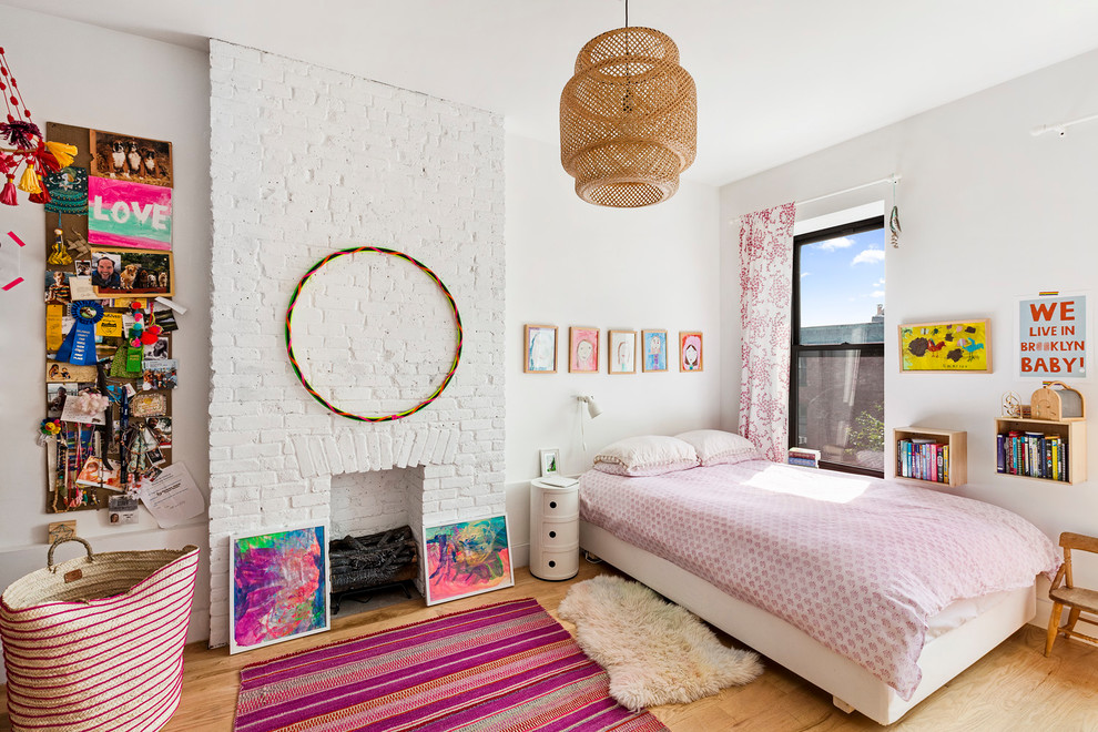 This is an example of an eclectic kids' room for girls in New York with white walls, light hardwood floors and beige floor.