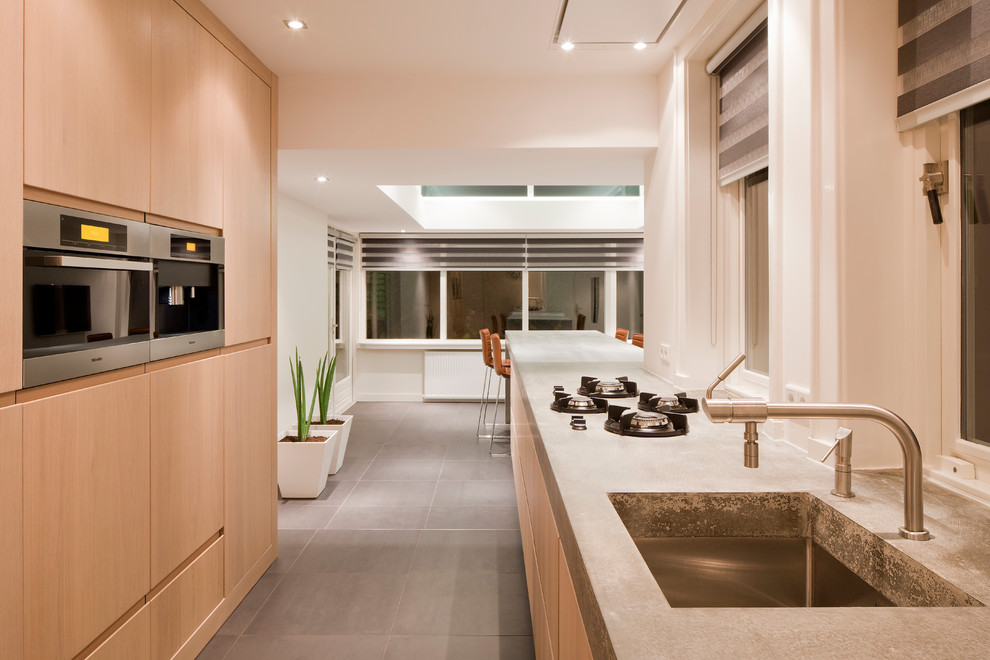 This is an example of a mid-sized contemporary galley separate kitchen in Brisbane with a farmhouse sink, light wood cabinets, concrete benchtops, black appliances, ceramic floors and with island.