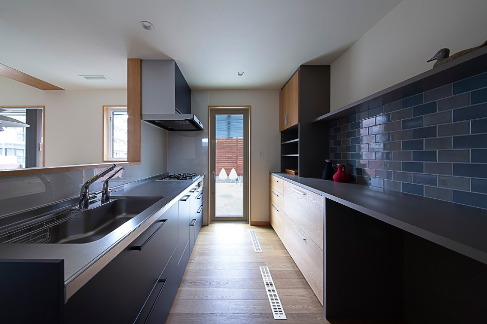 Exempel på ett mellanstort minimalistiskt grå linjärt grått kök med öppen planlösning, med släta luckor, blå skåp, bänkskiva i rostfritt stål, blått stänkskydd, stänkskydd i keramik, rostfria vitvaror, ljust trägolv och en halv köksö
