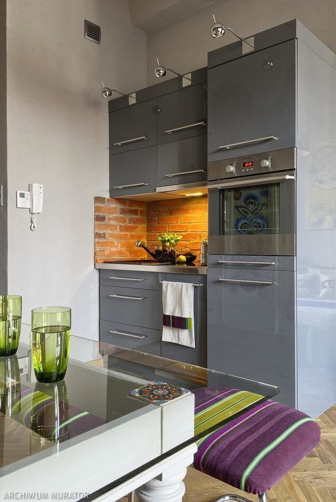 Contemporary single-wall eat-in kitchen in Moscow with flat-panel cabinets, grey cabinets, stainless steel benchtops, grey splashback, stainless steel appliances, light hardwood floors and no island.