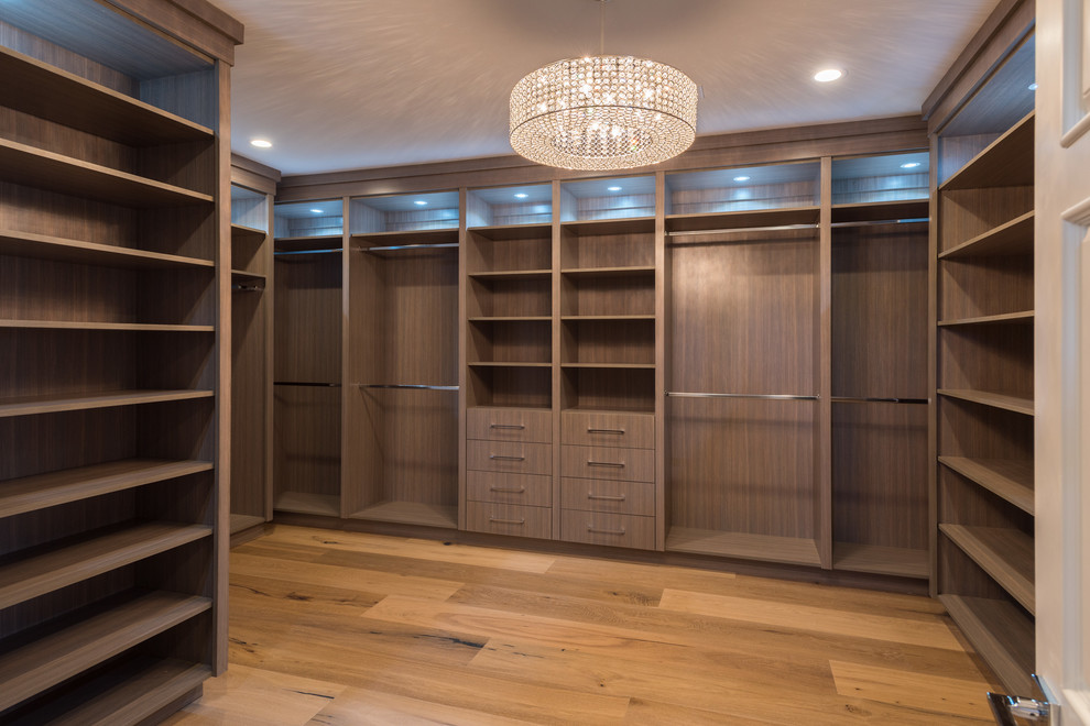 Expansive traditional gender-neutral dressing room in Los Angeles with flat-panel cabinets, medium wood cabinets, light hardwood floors and brown floor.