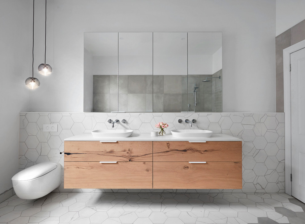 This is an example of a large contemporary master bathroom in Melbourne with flat-panel cabinets, light wood cabinets, a freestanding tub, an open shower, gray tile, white tile, mosaic tile, white walls, mosaic tile floors, a vessel sink and solid surface benchtops.