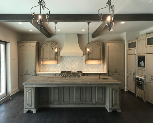 Rustic kitchen with large wood island, exposed beams and twin arched upper kitchen cabinets flanking the range hood