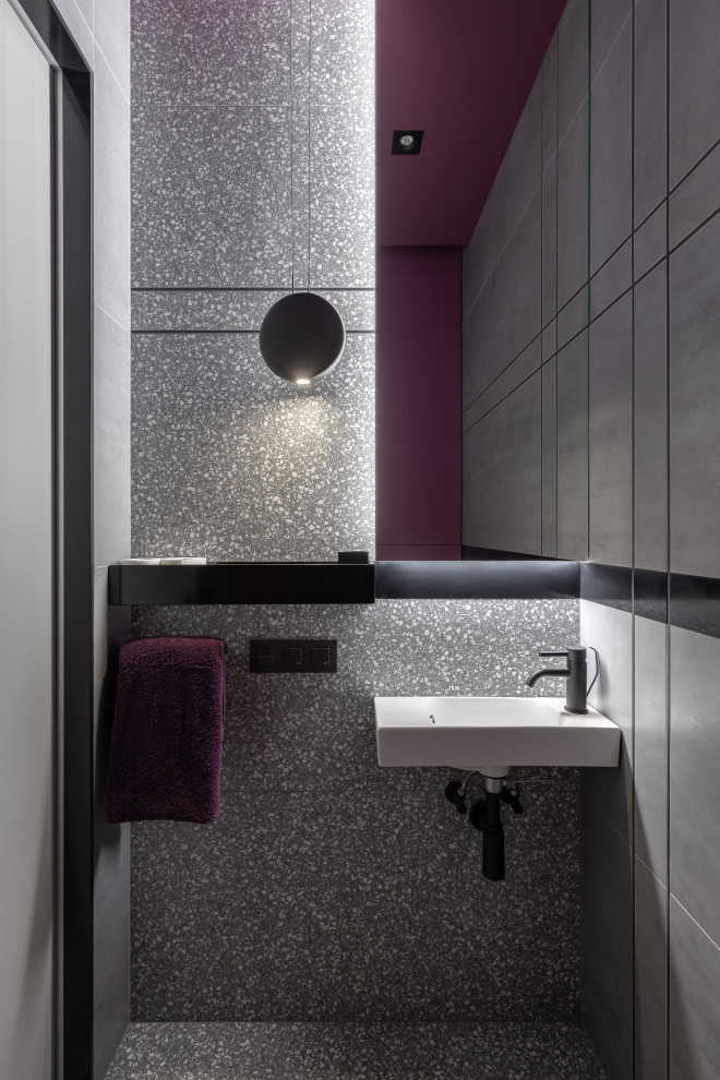 Photo of a small contemporary powder room in Saint Petersburg with a wall-mount toilet, gray tile, porcelain tile, purple walls, porcelain floors, a wall-mount sink and grey floor.