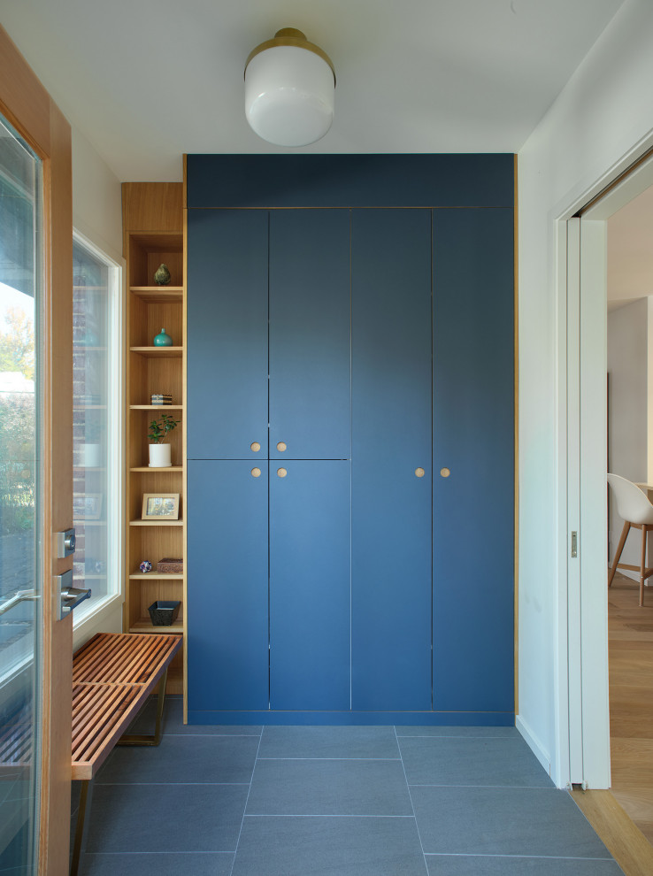This is an example of a mid-sized scandinavian mudroom in New York with white walls, light hardwood floors, a single front door, a light wood front door and grey floor.
