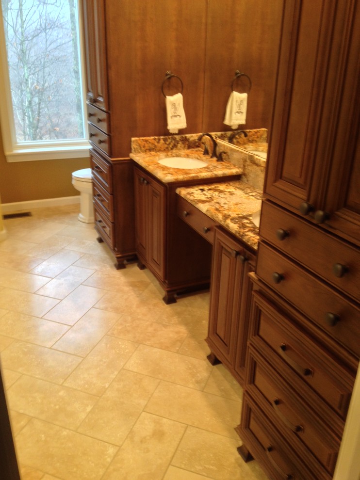 This is an example of a large traditional master bathroom in Charlotte with an undermount sink, furniture-like cabinets, medium wood cabinets, granite benchtops, a freestanding tub, an open shower, a one-piece toilet, beige tile, stone tile, beige walls and travertine floors.