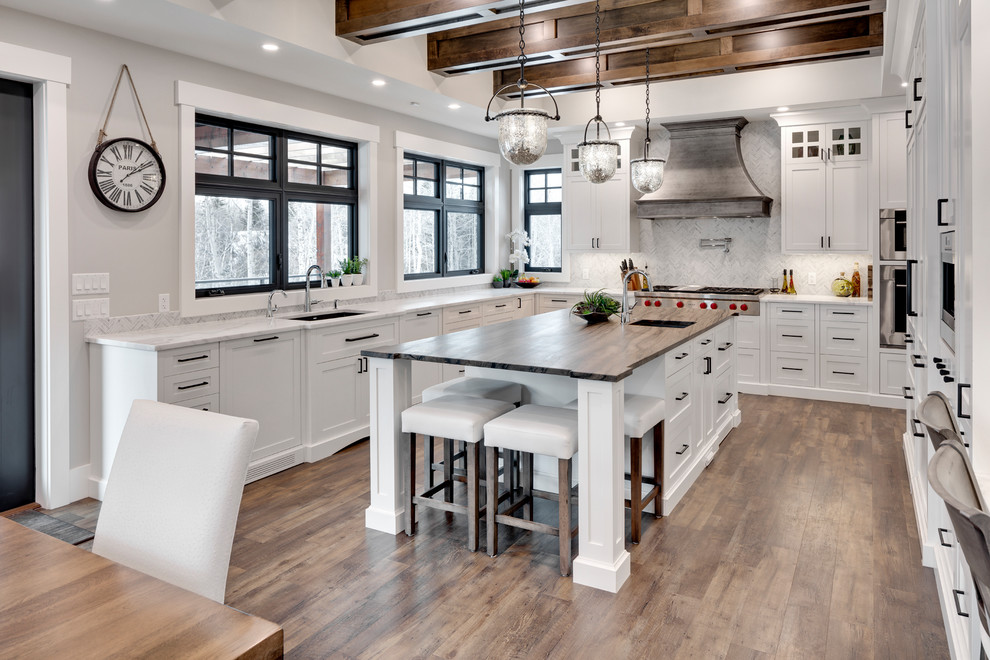 Example of a huge transitional u-shaped brown floor and medium tone wood floor kitchen design in Calgary with an undermount sink, shaker cabinets, white cabinets, marble countertops, white backsplash, marble backsplash, stainless steel appliances, an island and white countertops