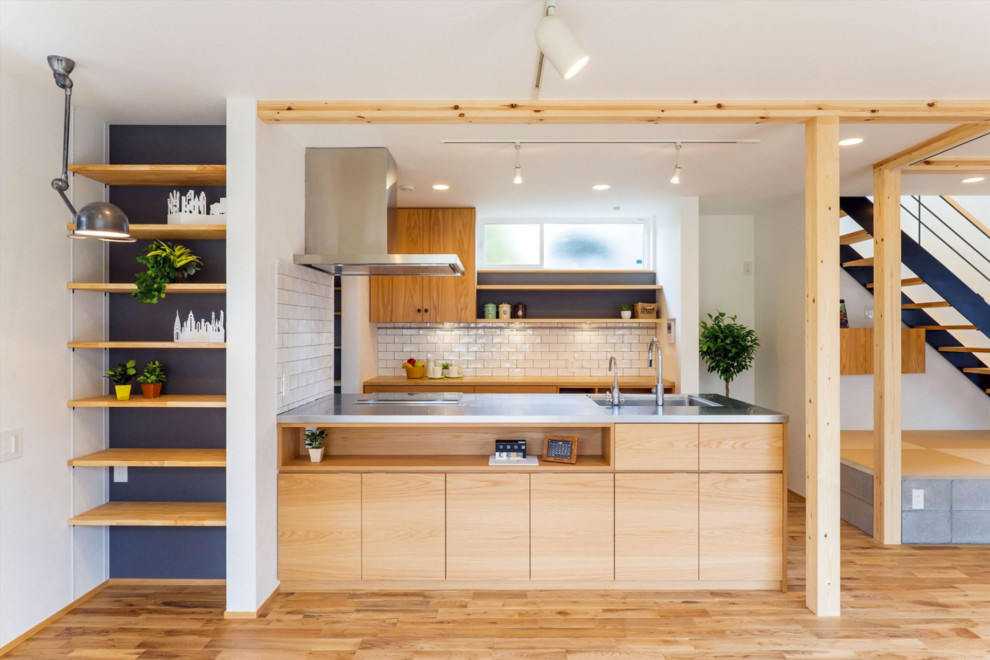 Photo of a contemporary single-wall kitchen in Tokyo Suburbs with a single-bowl sink, flat-panel cabinets, stainless steel benchtops, white splashback, stone tile splashback, light hardwood floors, with island and light wood cabinets.