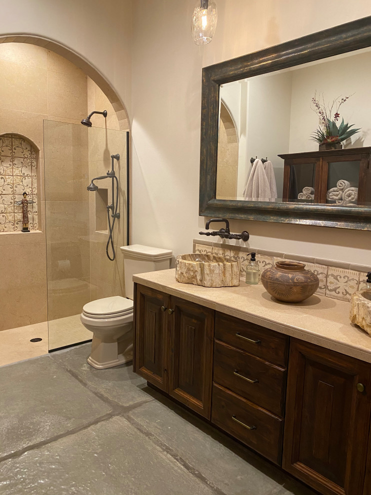 Photo of a medium sized rustic bathroom in Phoenix with raised-panel cabinets, brown cabinets, a built-in shower, a two-piece toilet, beige tiles, limestone tiles, white walls, concrete flooring, a vessel sink, limestone worktops, grey floors, an open shower, beige worktops, a wall niche, double sinks and a built in vanity unit.