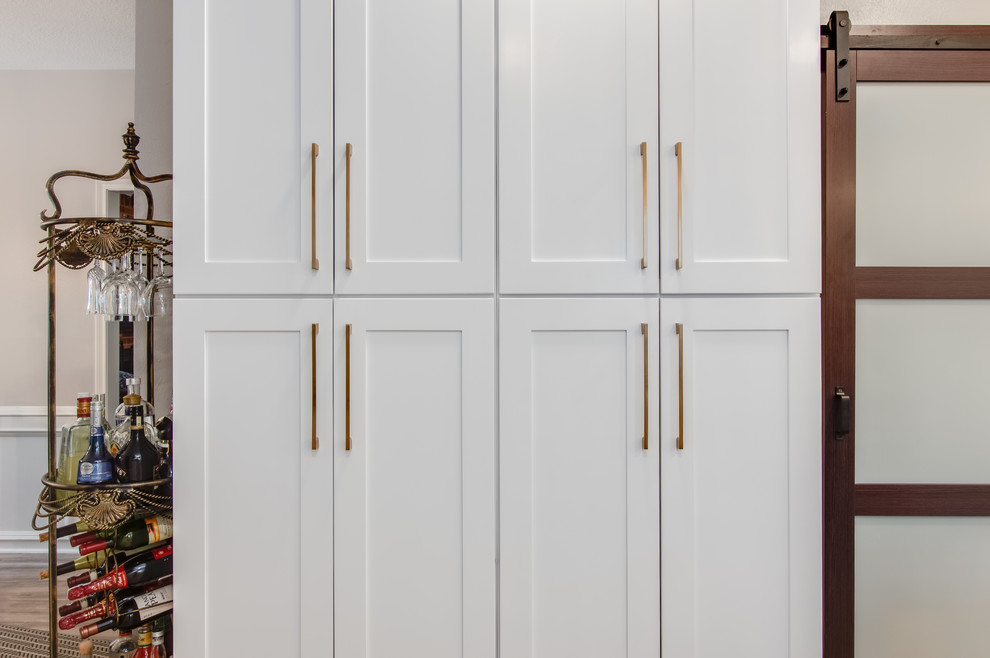 Inspiration for a large transitional l-shaped porcelain tile and gray floor kitchen pantry remodel in Houston with a farmhouse sink, shaker cabinets, white cabinets, quartzite countertops, white backsplash, glass tile backsplash, stainless steel appliances, an island and white countertops