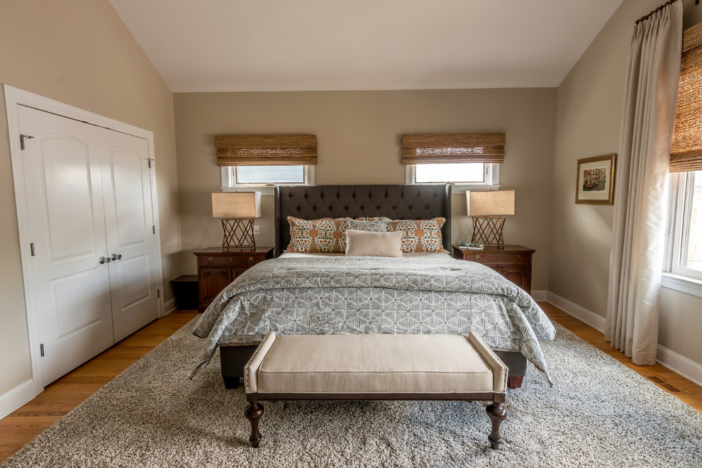 This is an example of a mid-sized transitional master bedroom in Chicago with beige walls, medium hardwood floors, a corner fireplace, a stone fireplace surround and orange floor.