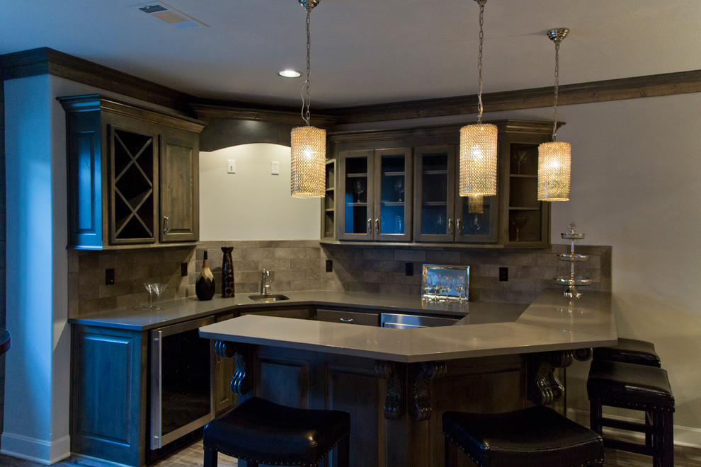This is an example of a mid-sized modern u-shaped seated home bar in Kansas City with an undermount sink, glass-front cabinets, grey cabinets, grey splashback, ceramic splashback, medium hardwood floors and grey floor.