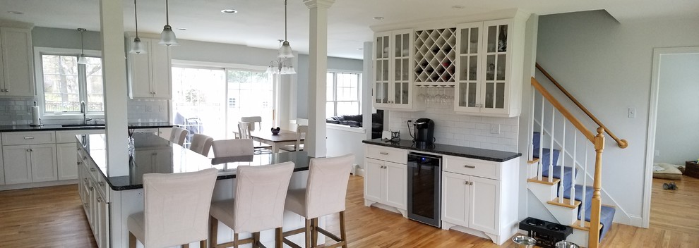 Inspiration for a large transitional l-shaped light wood floor and brown floor eat-in kitchen remodel with an undermount sink, shaker cabinets, white cabinets, granite countertops, white backsplash, subway tile backsplash, stainless steel appliances and an island