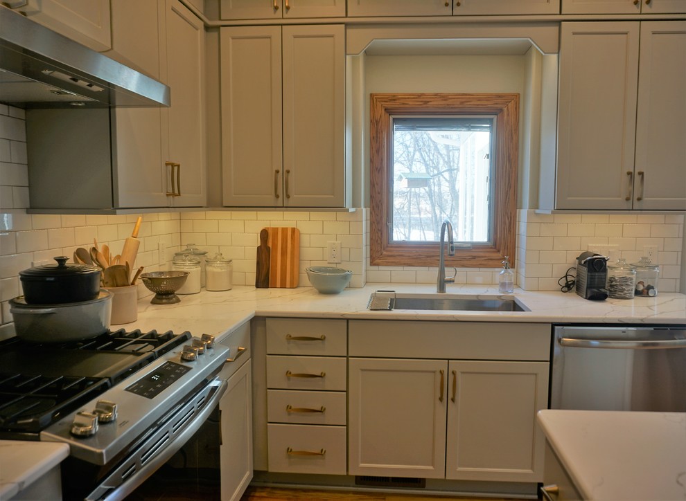 Transitional l-shaped medium tone wood floor eat-in kitchen photo with an undermount sink, recessed-panel cabinets, gray cabinets, quartz countertops, white backsplash, ceramic backsplash, stainless steel appliances, an island and white countertops