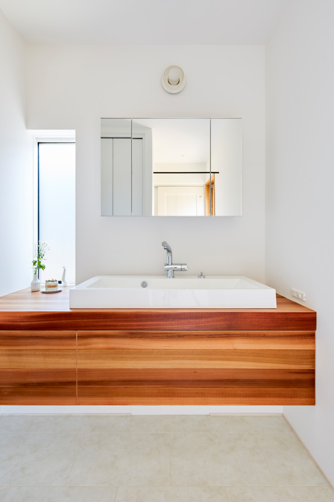 Inspiration for a mid-sized asian powder room in Other with flat-panel cabinets, white walls, porcelain floors, a vessel sink, wood benchtops, beige floor and brown benchtops.
