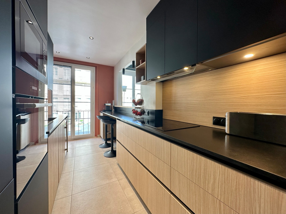 Inspiration for a mid-sized modern galley separate kitchen in Le Havre with an integrated sink, beaded inset cabinets, light wood cabinets, granite benchtops, timber splashback, black appliances, ceramic floors, no island, beige floor and black benchtop.