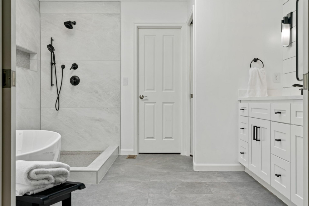 На фото: ванная комната с белыми фасадами, отдельно стоящей ванной, душем без бортиков, унитазом-моноблоком, белой плиткой, белыми стенами, мраморным полом, серым полом, открытым душем, белой столешницей, тумбой под две раковины и напольной тумбой с