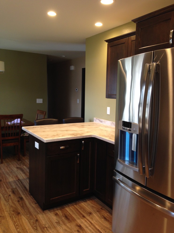 Mid-sized mountain style open concept kitchen photo with an integrated sink, flat-panel cabinets, dark wood cabinets, solid surface countertops, stainless steel appliances and a peninsula