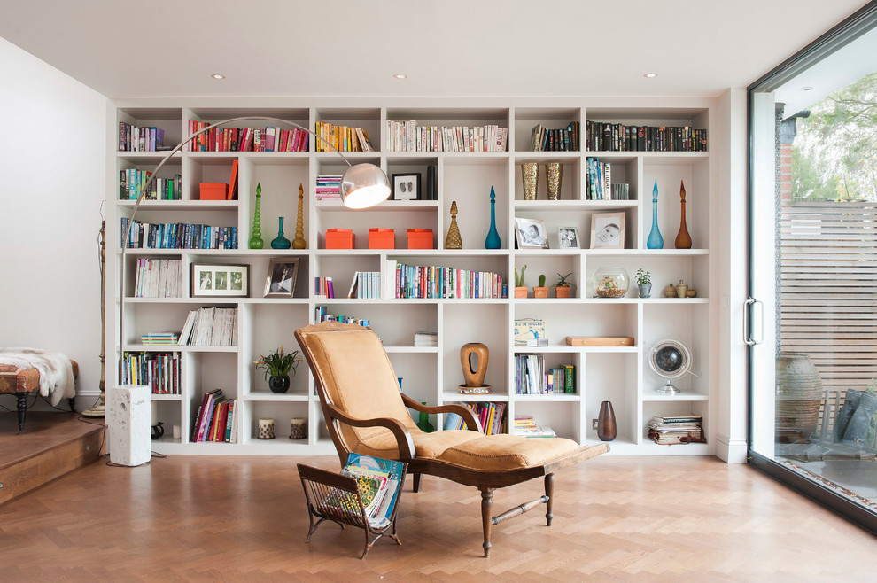 This is an example of a contemporary open concept living room in London with a library and light hardwood floors.