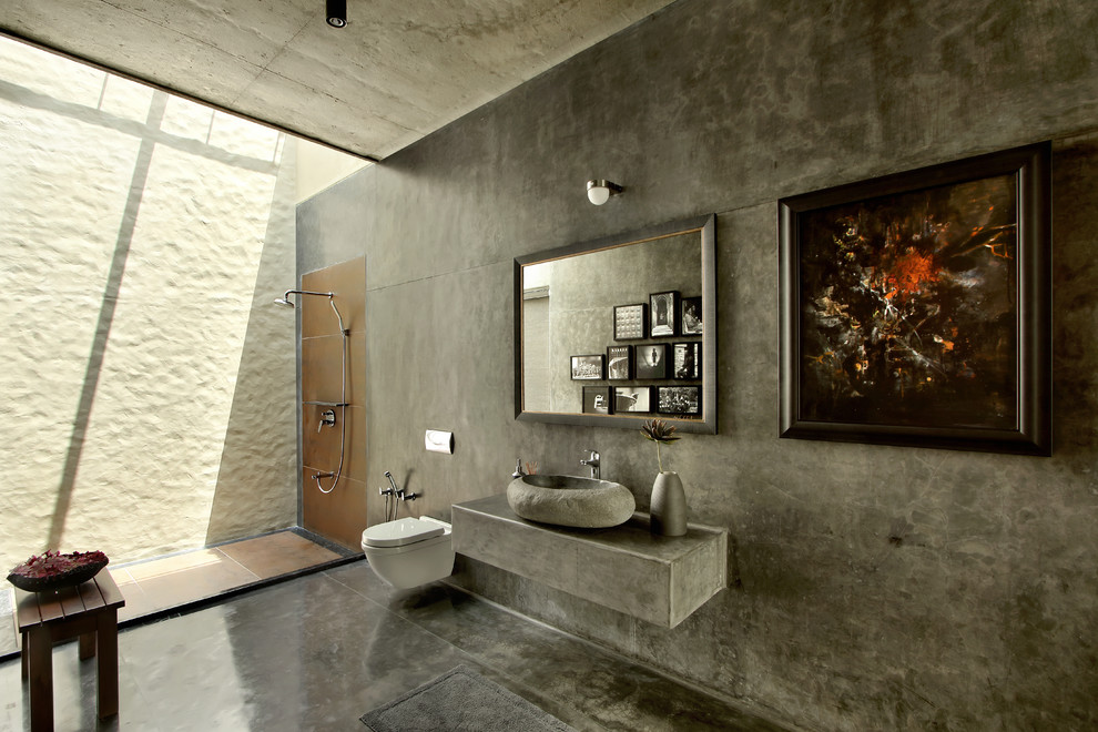 This is an example of a tropical bathroom in Ahmedabad with an open shower, a wall-mount toilet, concrete floors, a vessel sink, grey walls and an open shower.