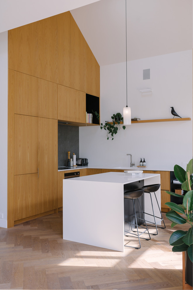This is an example of a contemporary l-shaped kitchen in Auckland with flat-panel cabinets, medium wood cabinets, light hardwood floors, with island, beige floor and white benchtop.