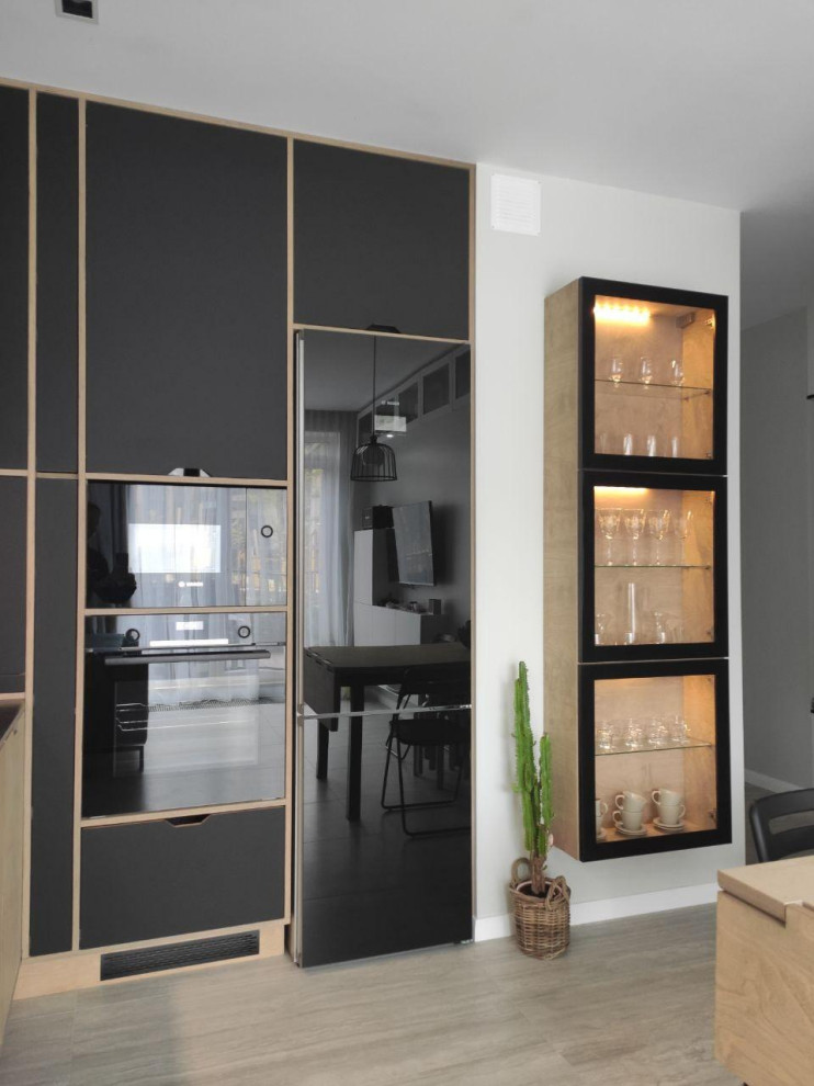 This is an example of a mid-sized industrial l-shaped eat-in kitchen in Other with an undermount sink, flat-panel cabinets, black cabinets, tile benchtops, white splashback, subway tile splashback, black appliances, ceramic floors, grey floor and black benchtop.