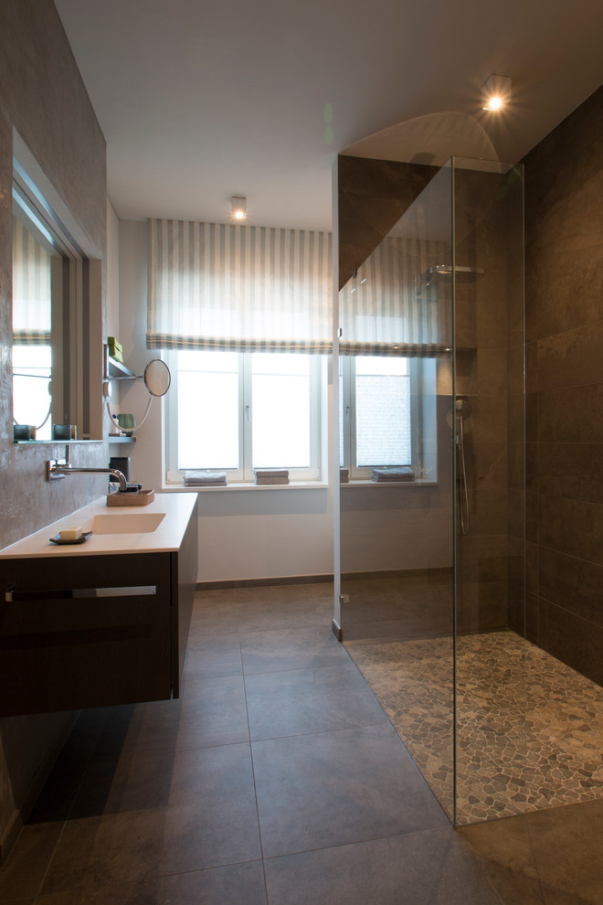 Duschbad With flächenbündigen Schrankfronten, braunen Schränken, bodengleicher Dusche, Wandtoilette, braunen Fliesen, Steinfliesen, weißer Wandfarbe, Mosaik-Bodenfliesen, integriertem Waschbecken and Mineralwerkstoff-Waschtisch in Berlin