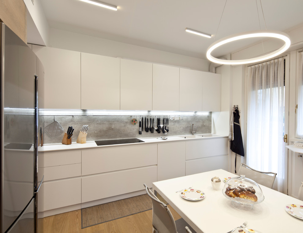 Mid-sized contemporary single-wall separate kitchen in Milan with an integrated sink, beaded inset cabinets, white cabinets, laminate benchtops, grey splashback, timber splashback, stainless steel appliances, light hardwood floors, no island, beige floor and white benchtop.