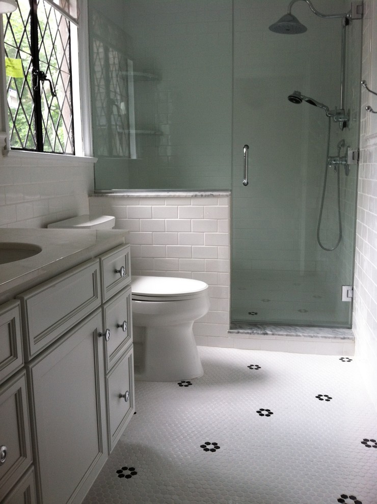 This is an example of a small traditional bathroom in Philadelphia with recessed-panel cabinets, white cabinets, solid surface benchtops, white tile, ceramic tile, an alcove shower, a two-piece toilet, an undermount sink, white walls and mosaic tile floors.