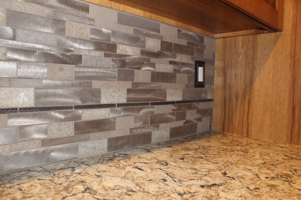 Example of a large mountain style l-shaped medium tone wood floor and brown floor open concept kitchen design with an undermount sink, raised-panel cabinets, brown cabinets, quartzite countertops, metallic backsplash, black appliances, an island and brown countertops