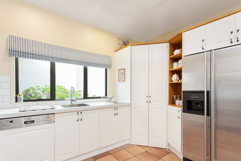 Small country u-shaped separate kitchen in Christchurch with a single-bowl sink, recessed-panel cabinets, white cabinets, white splashback, ceramic splashback, stainless steel appliances, terra-cotta floors, no island, orange floor and white benchtop.