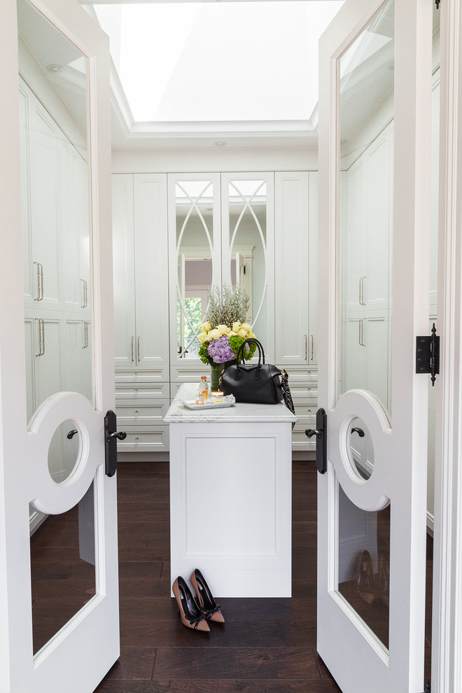 This is an example of a large traditional women's dressing room in Toronto with white cabinets, dark hardwood floors, brown floor and glass-front cabinets.