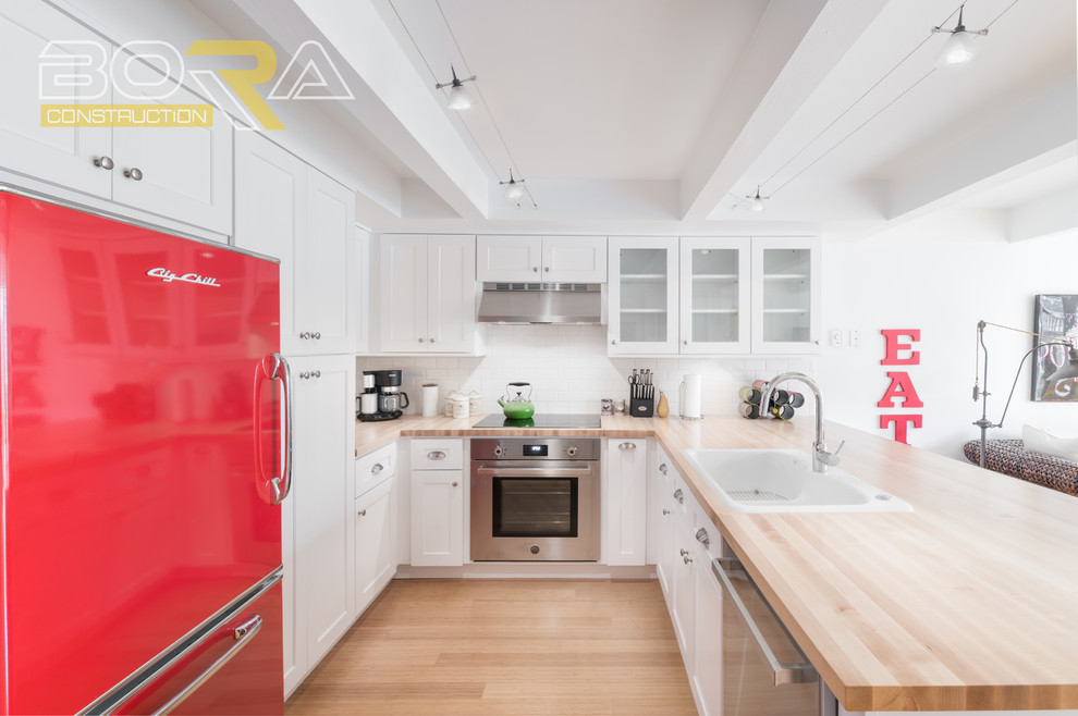 Example of a small transitional u-shaped medium tone wood floor and beige floor eat-in kitchen design with a double-bowl sink, shaker cabinets, white cabinets, wood countertops, white backsplash, ceramic backsplash, stainless steel appliances and a peninsula