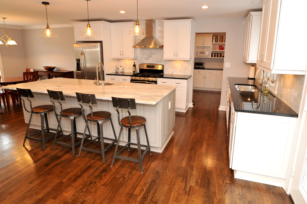 Example of a mid-sized transitional l-shaped medium tone wood floor open concept kitchen design in Atlanta with a double-bowl sink, white cabinets, quartzite countertops, white backsplash, stainless steel appliances and an island