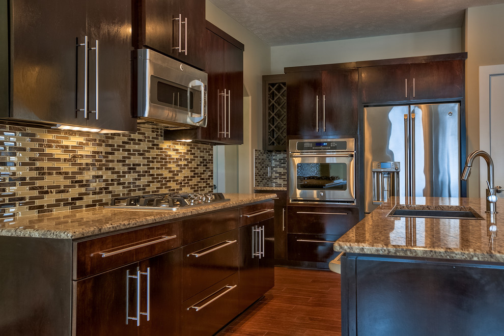 Photo of a mid-sized contemporary galley eat-in kitchen in Omaha with an undermount sink, flat-panel cabinets, dark wood cabinets, granite benchtops, beige splashback, glass tile splashback, stainless steel appliances, medium hardwood floors and with island.