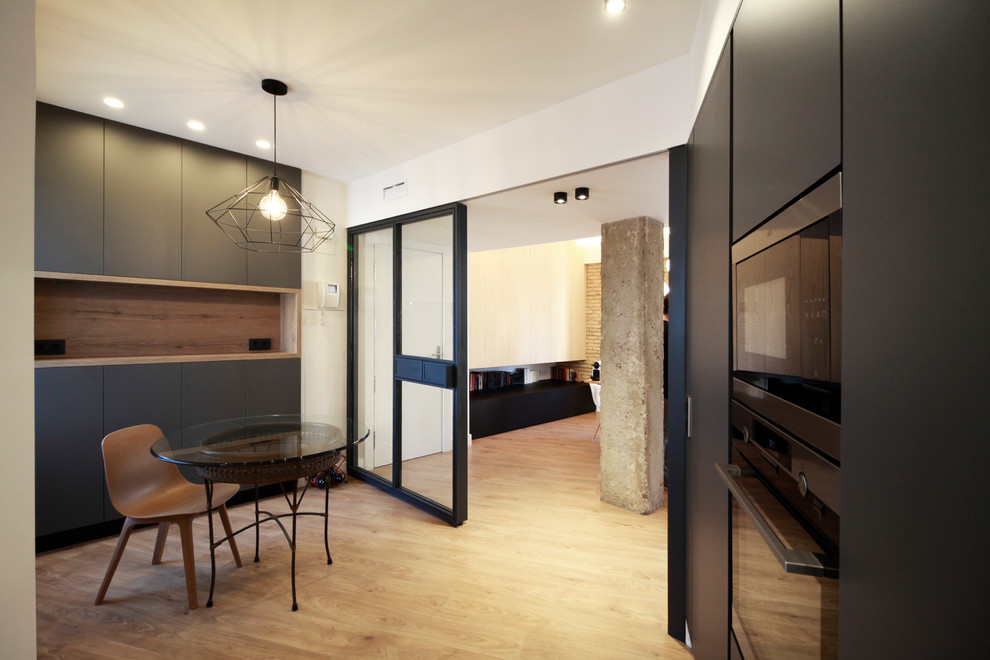 This is an example of a mid-sized contemporary u-shaped eat-in kitchen in Other with an undermount sink, flat-panel cabinets, black cabinets, white splashback, panelled appliances and laminate floors.