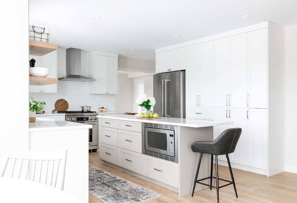 Example of a large transitional u-shaped medium tone wood floor and brown floor eat-in kitchen design in Calgary with an undermount sink, shaker cabinets, white cabinets, quartzite countertops, white backsplash, subway tile backsplash, stainless steel appliances, an island and white countertops