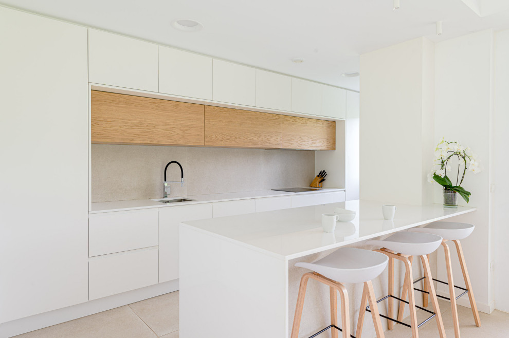 This is an example of a contemporary single-wall open plan kitchen in Other with a submerged sink, flat-panel cabinets, white cabinets, engineered stone countertops, beige splashback, ceramic splashback, integrated appliances, ceramic flooring, an island, beige floors and white worktops.