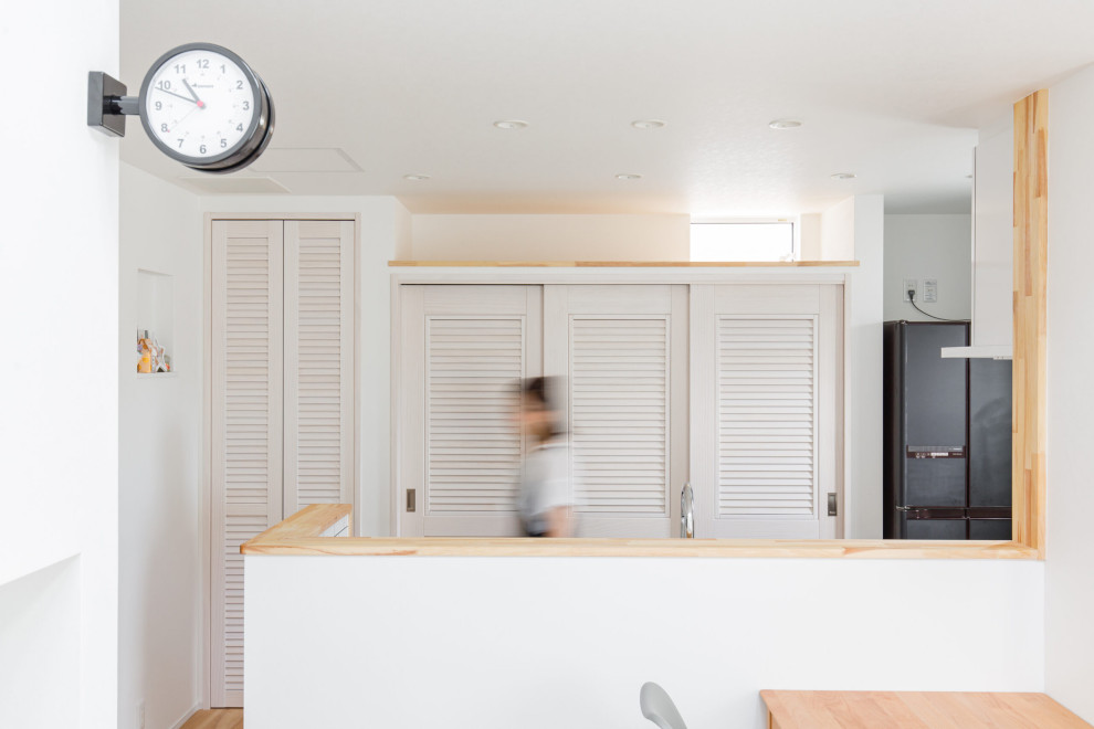 Inspiration för ett maritimt grå linjärt grått kök med öppen planlösning, med vita skåp, en köksö, en undermonterad diskho, luckor med lamellpanel, vitt stänkskydd, svarta vitvaror, mellanmörkt trägolv och brunt golv