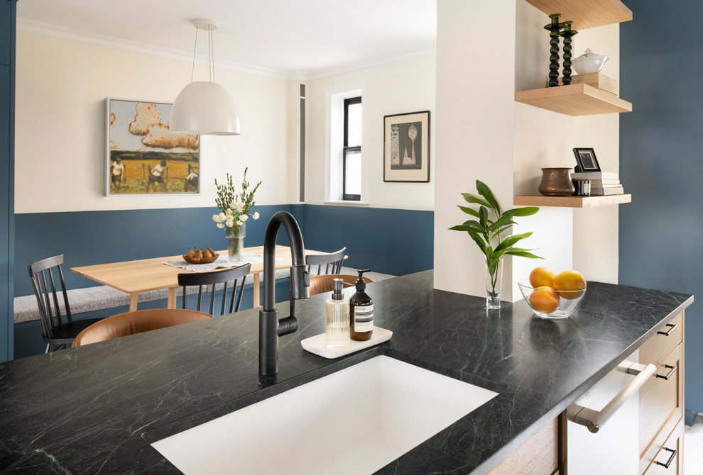 Photo of a mid-sized transitional galley eat-in kitchen in New York with an undermount sink, shaker cabinets, light wood cabinets, soapstone benchtops, white splashback, ceramic splashback, stainless steel appliances, concrete floors, with island, white floor and black benchtop.