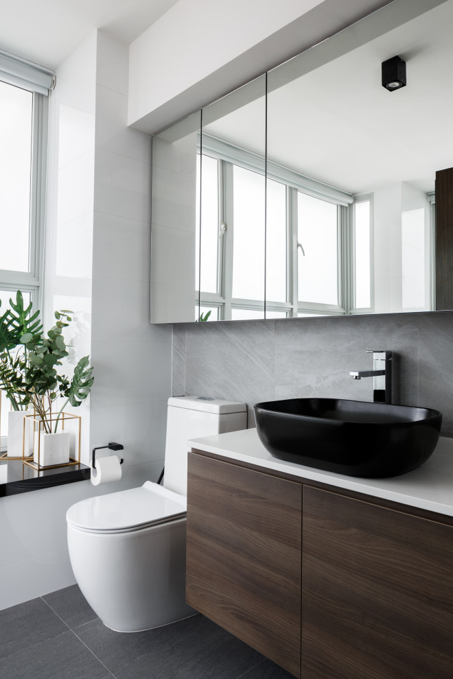 Mid-sized contemporary 3/4 bathroom in Singapore with flat-panel cabinets, medium wood cabinets, a two-piece toilet, gray tile, white walls, a vessel sink, grey floor and white benchtops.