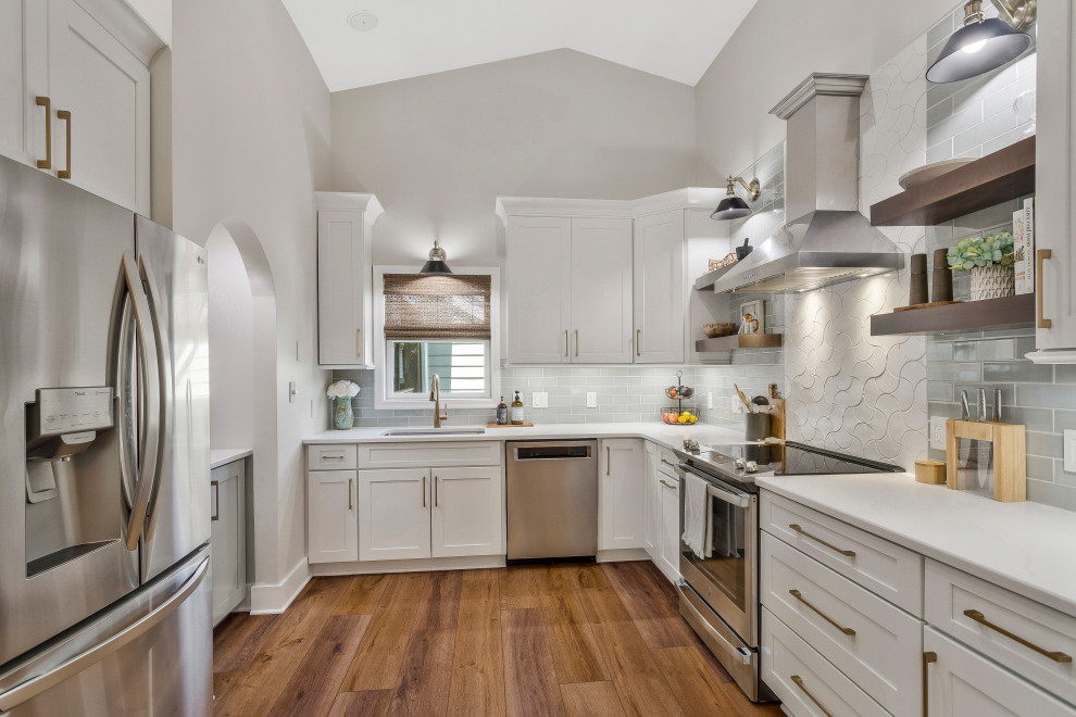 Photo of a large beach style u-shaped kitchen in DC Metro with an undermount sink, recessed-panel cabinets, white cabinets, quartz benchtops, grey splashback, subway tile splashback, stainless steel appliances, no island and white benchtop.
