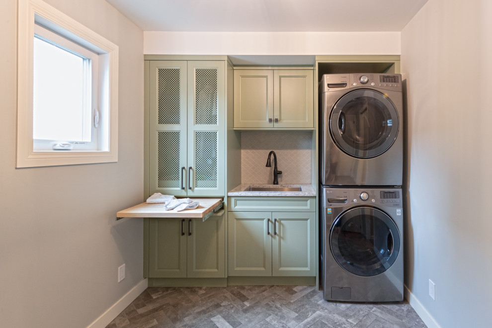 Photo of a mid-sized traditional galley dedicated laundry room in Edmonton with a single-bowl sink, recessed-panel cabinets, green cabinets, quartz benchtops, grey splashback, ceramic splashback, grey walls, ceramic floors, a stacked washer and dryer, multi-coloured floor and multi-coloured benchtop.