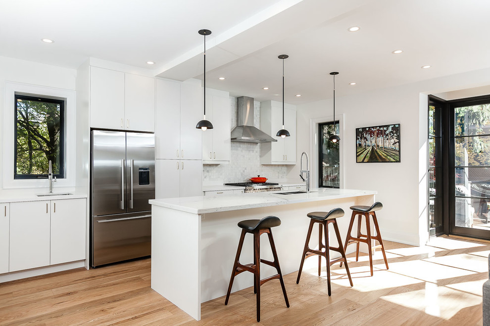 Photo of a contemporary galley kitchen in Toronto with flat-panel cabinets, white cabinets, white splashback, stainless steel appliances, medium hardwood floors and with island.
