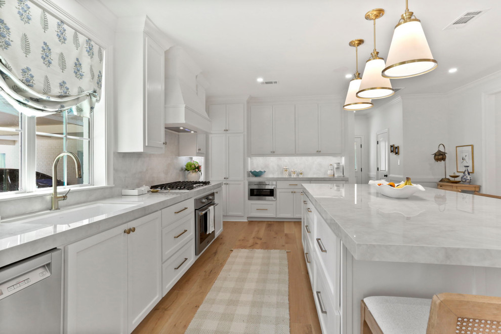 Open concept kitchen - large transitional l-shaped light wood floor and brown floor open concept kitchen idea in New Orleans with an undermount sink, shaker cabinets, white cabinets, quartz countertops, white backsplash, quartz backsplash, stainless steel appliances, an island and white countertops