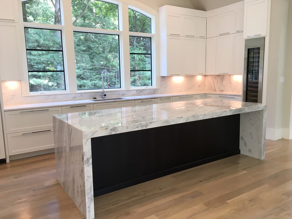 Design ideas for a mid-sized contemporary l-shaped open plan kitchen in Nashville with an undermount sink, flat-panel cabinets, white cabinets, quartzite benchtops, white splashback, stone slab splashback, stainless steel appliances, light hardwood floors and with island.
